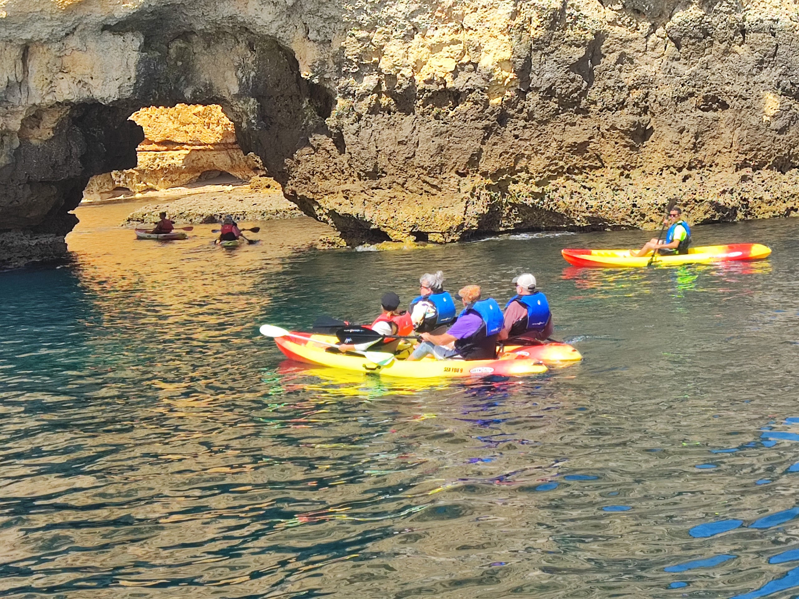 People kayaking near rocky arch formations in the water.