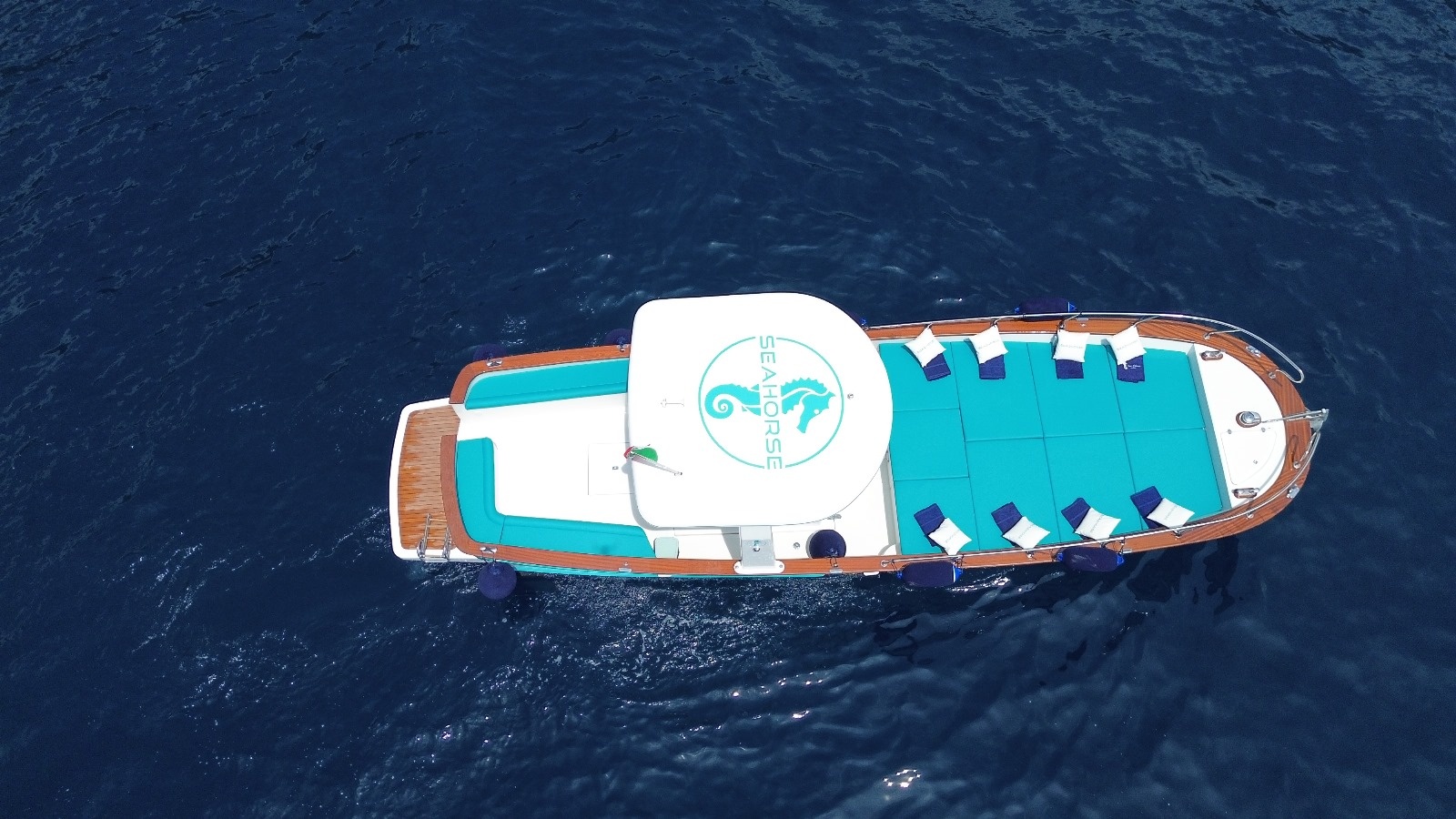 Aerial view of a boat with turquoise cushions on deep blue water.