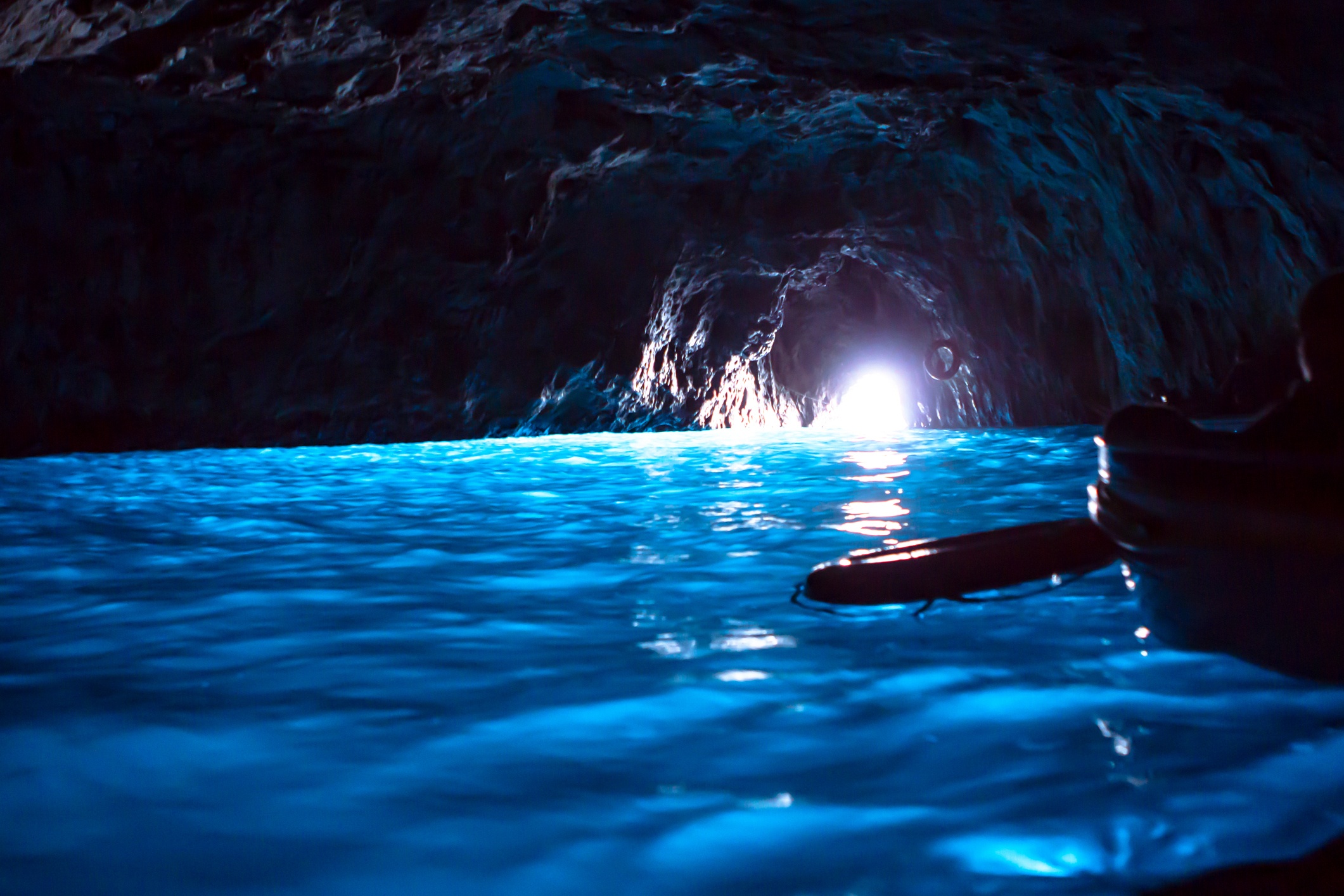 Sunlight illuminates a blue cave with reflective water.
