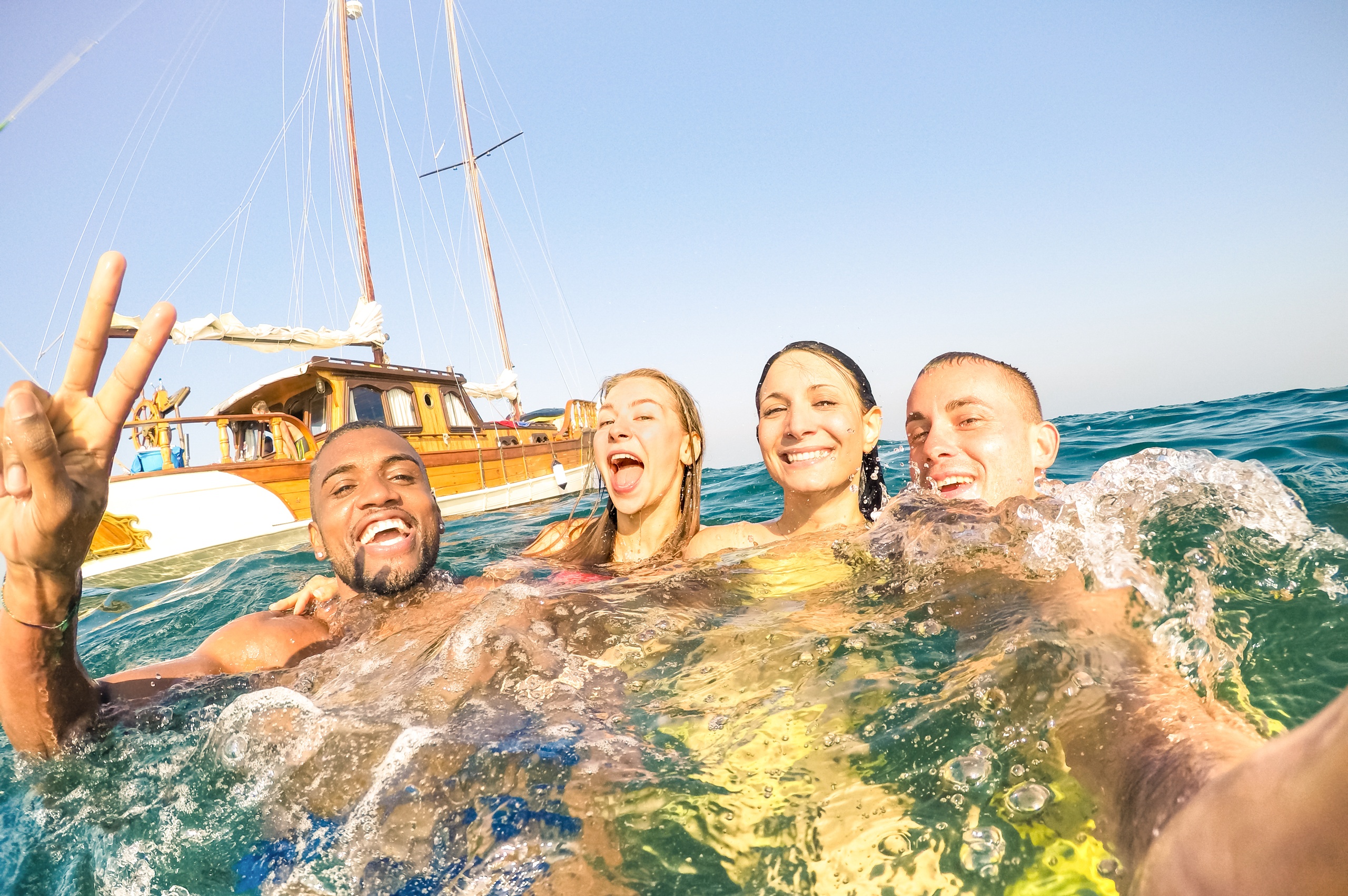 Four people smiling in water with a boat in the background.