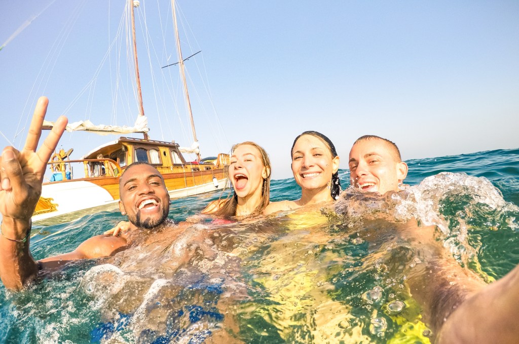 Four people smiling in water with a boat in the background.
