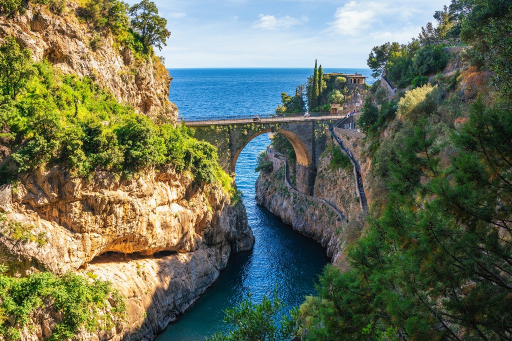 Historic bridge over a narrow canyon with clear blue water and rocky cliffs.