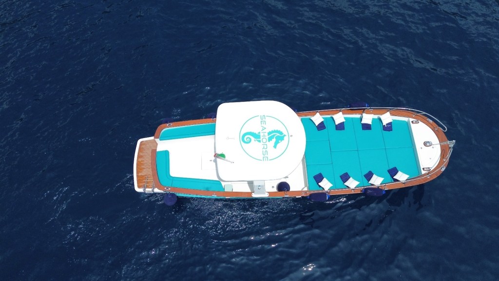 Aerial view of a boat with turquoise seating areas on a dark blue sea.