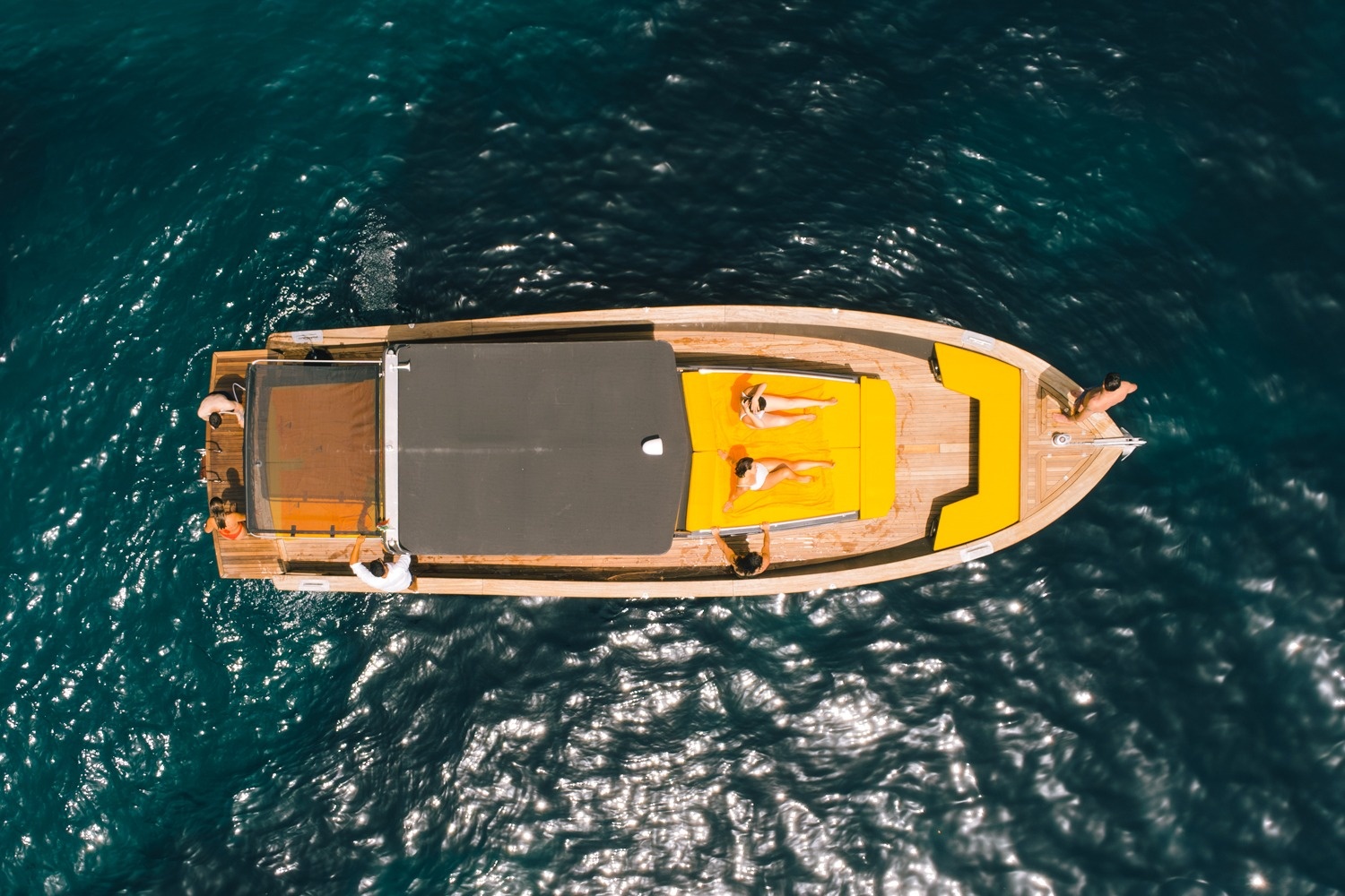 Aerial view of two people sunbathing on a boat in the ocean.