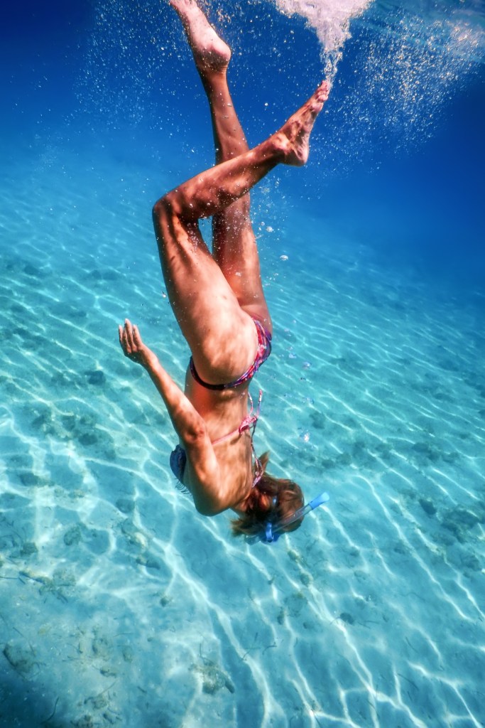Person diving underwater in clear blue sea, wearing a swimsuit and mask.