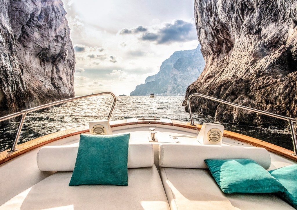 Boat with teal cushions in rocky coastal scenery with cloudy sky.