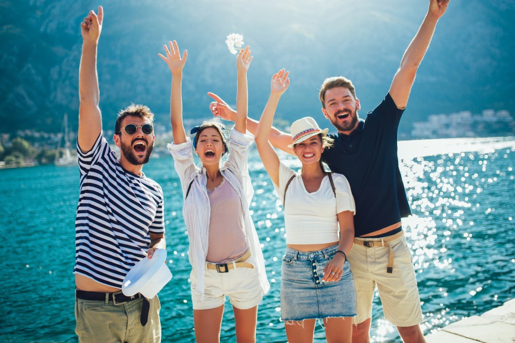 Four people cheerfully raising arms by a lakeside or seaside.
