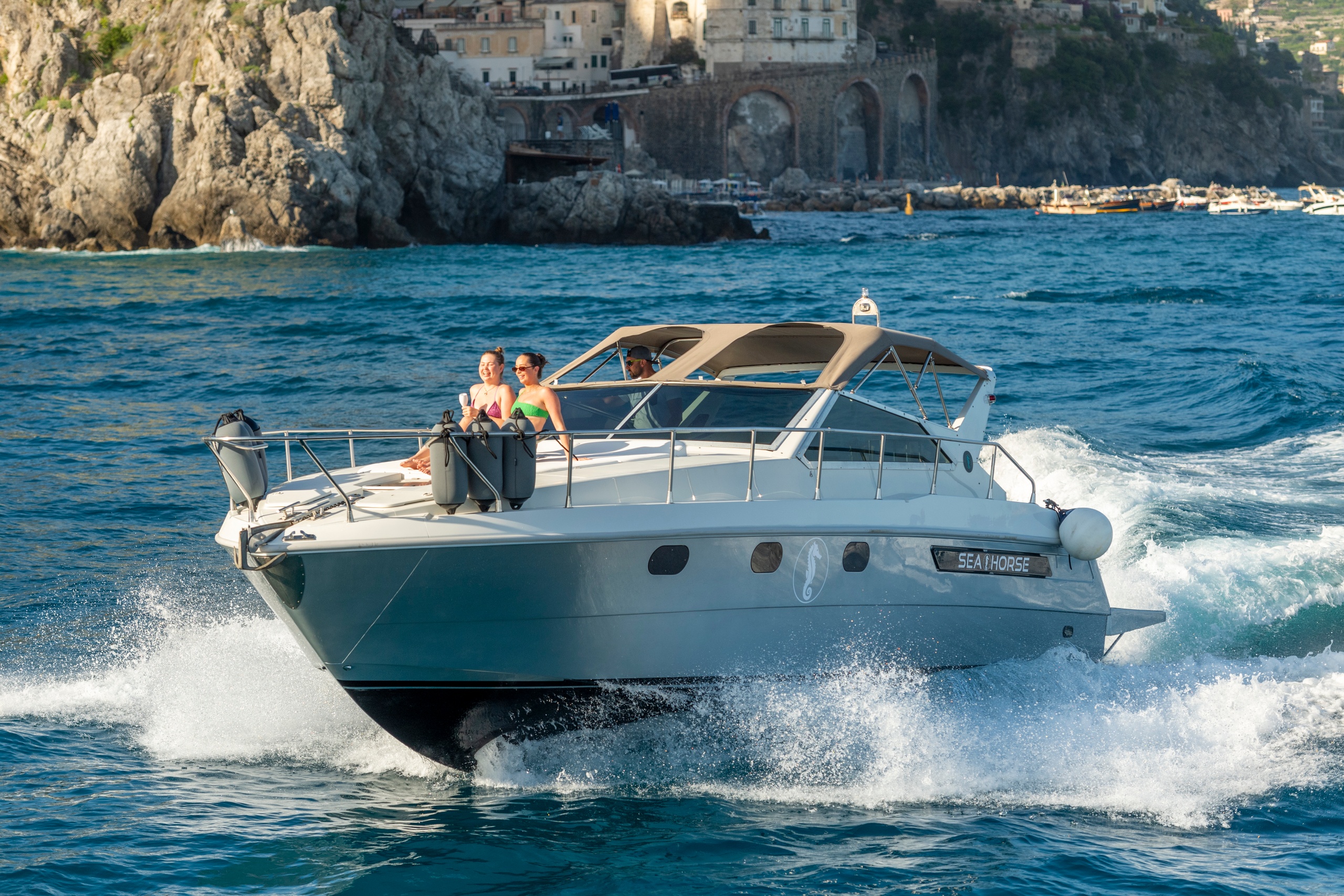 Motorboat with people cruising near rocky coast and buildings.