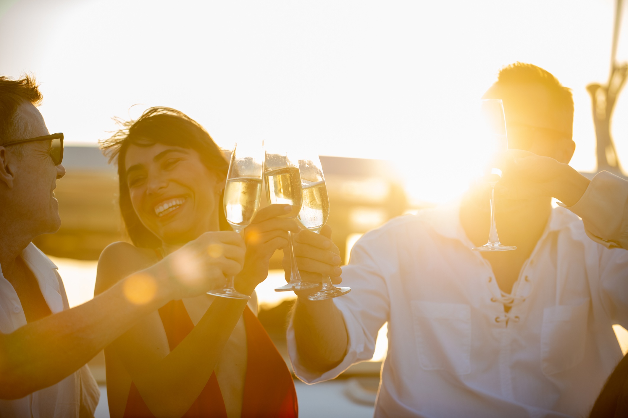 Three people toasting with champagne glasses on a boat at sunset.