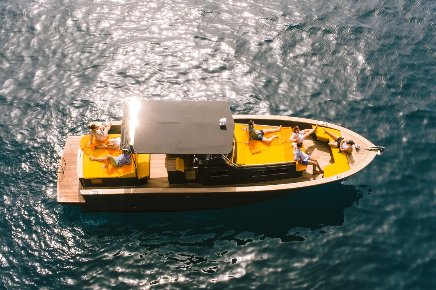 Aerial view of people relaxing on a boat with orange seating on water.