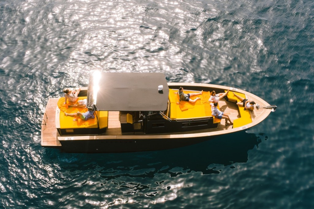 Aerial view of people relaxing on a boat with orange seating on water.