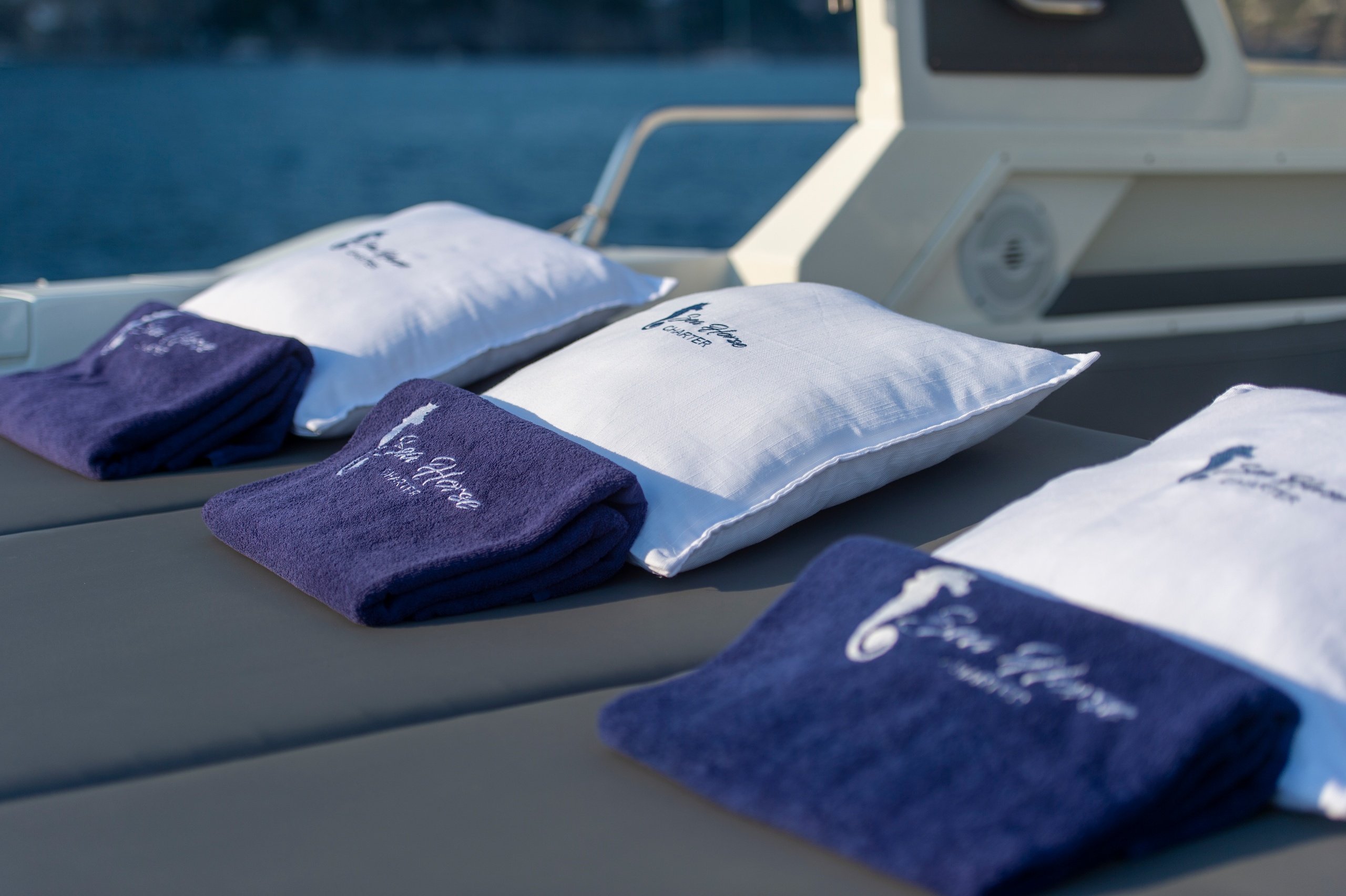 Three pillows with navy towels on a boat deck overlooking water.
