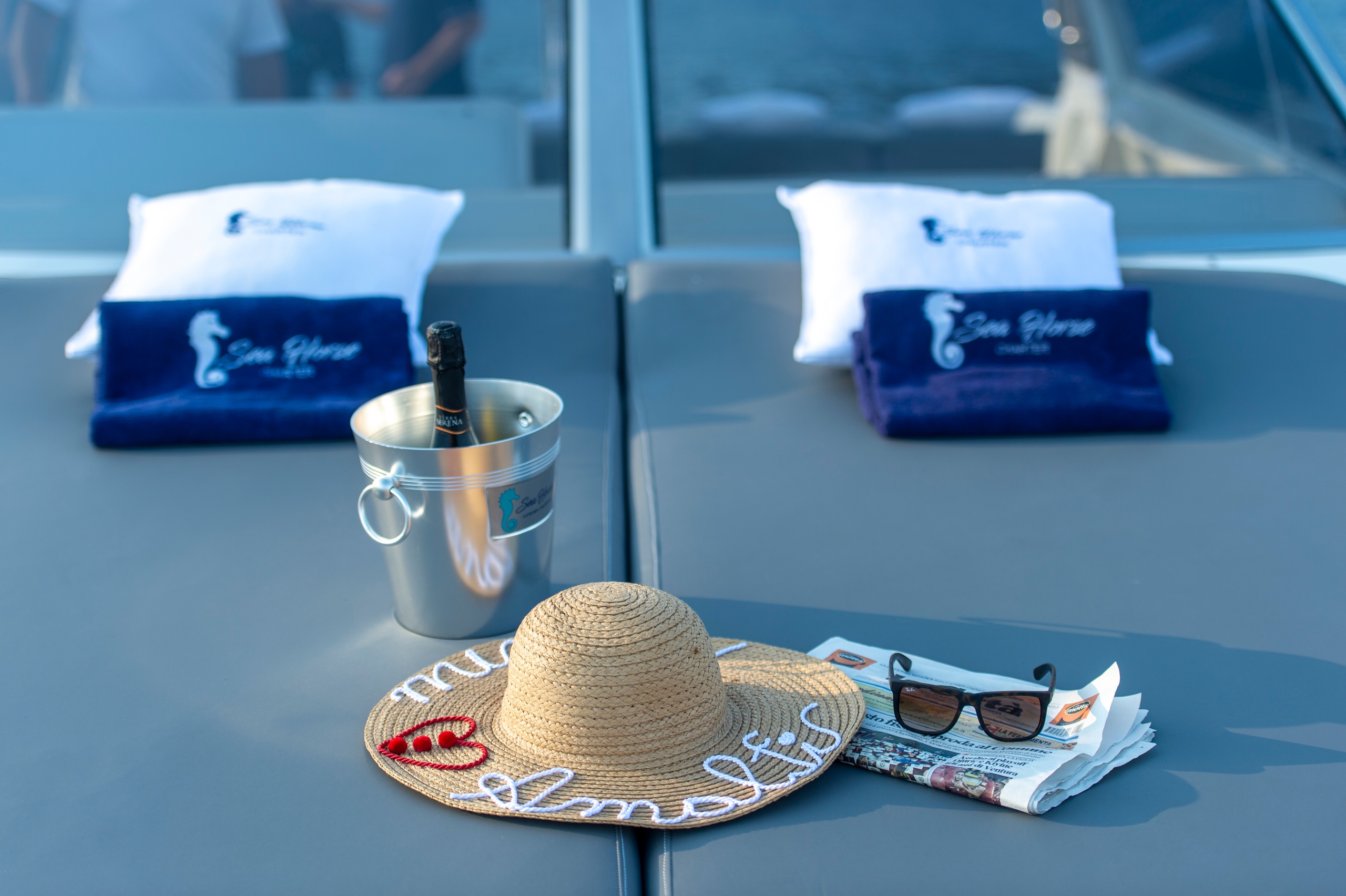 Beach items on yacht deck: straw hat, sunglasses, champagne in bucket, towels.