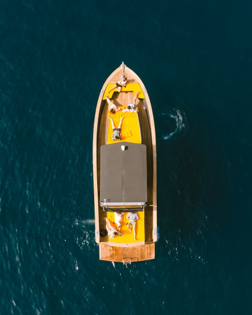 Aerial view of a boat with people sunbathing on bright yellow cushions.