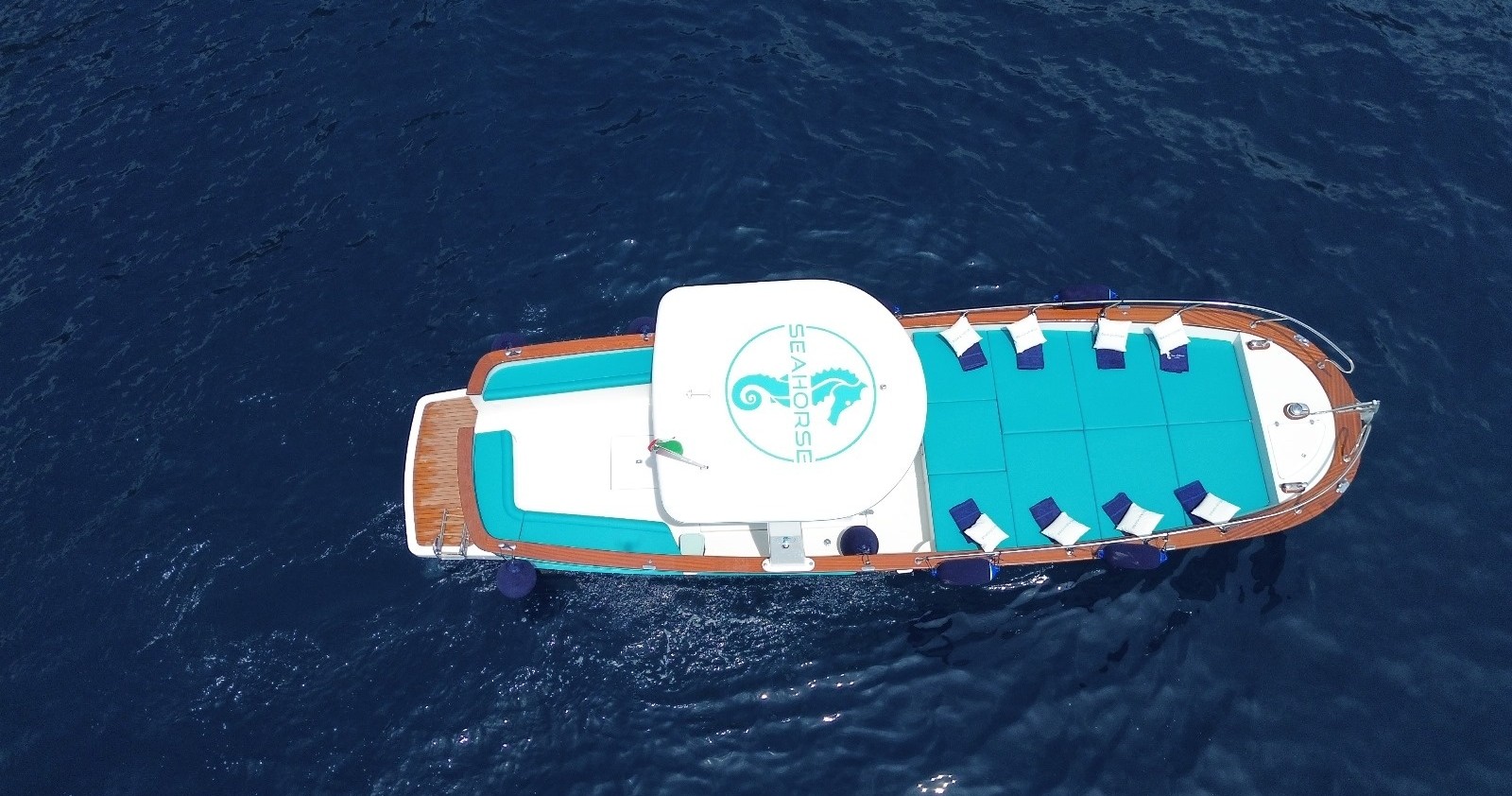 Aerial view of a boat with blue and white deck on deep blue water.