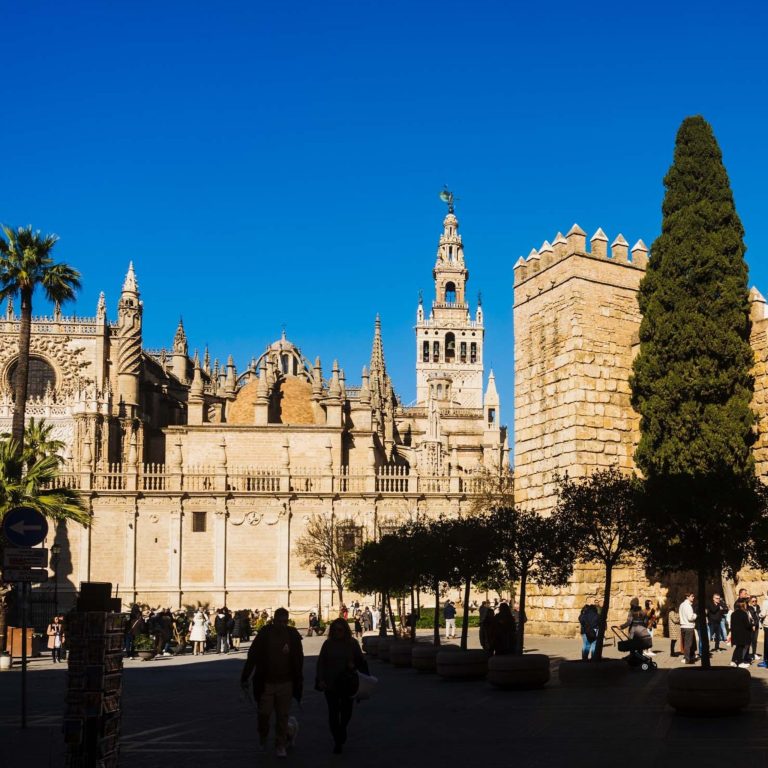 Large historic cathedral with tall tower and people walking below on a sunny day.