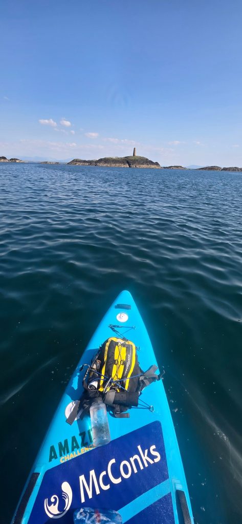 Paddleboarder on calm water, distant lighthouse on horizon.