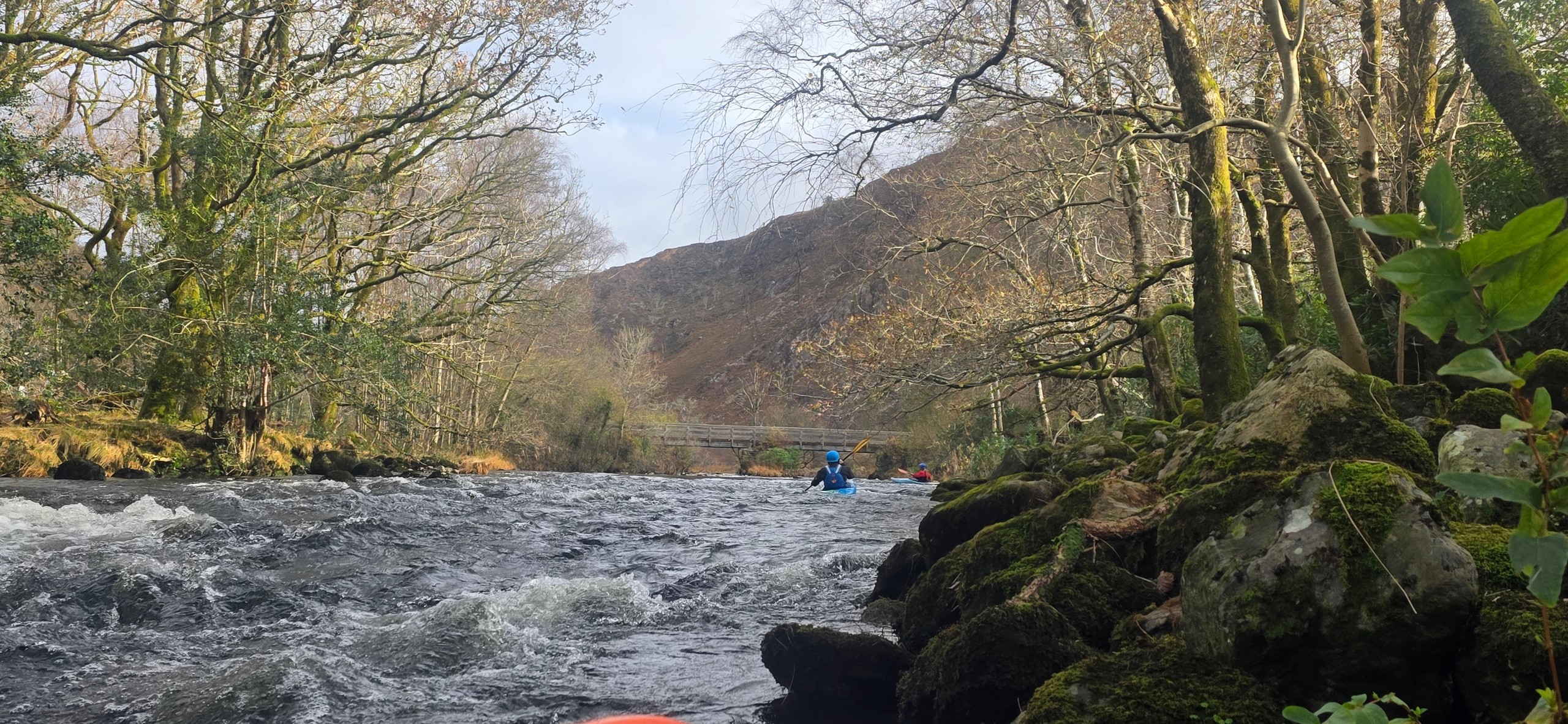 Kayakers on a river surrounded by bare trees and hills.