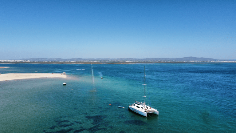 Sailboat anchored in calm blue sea near sandy shore under clear sky.