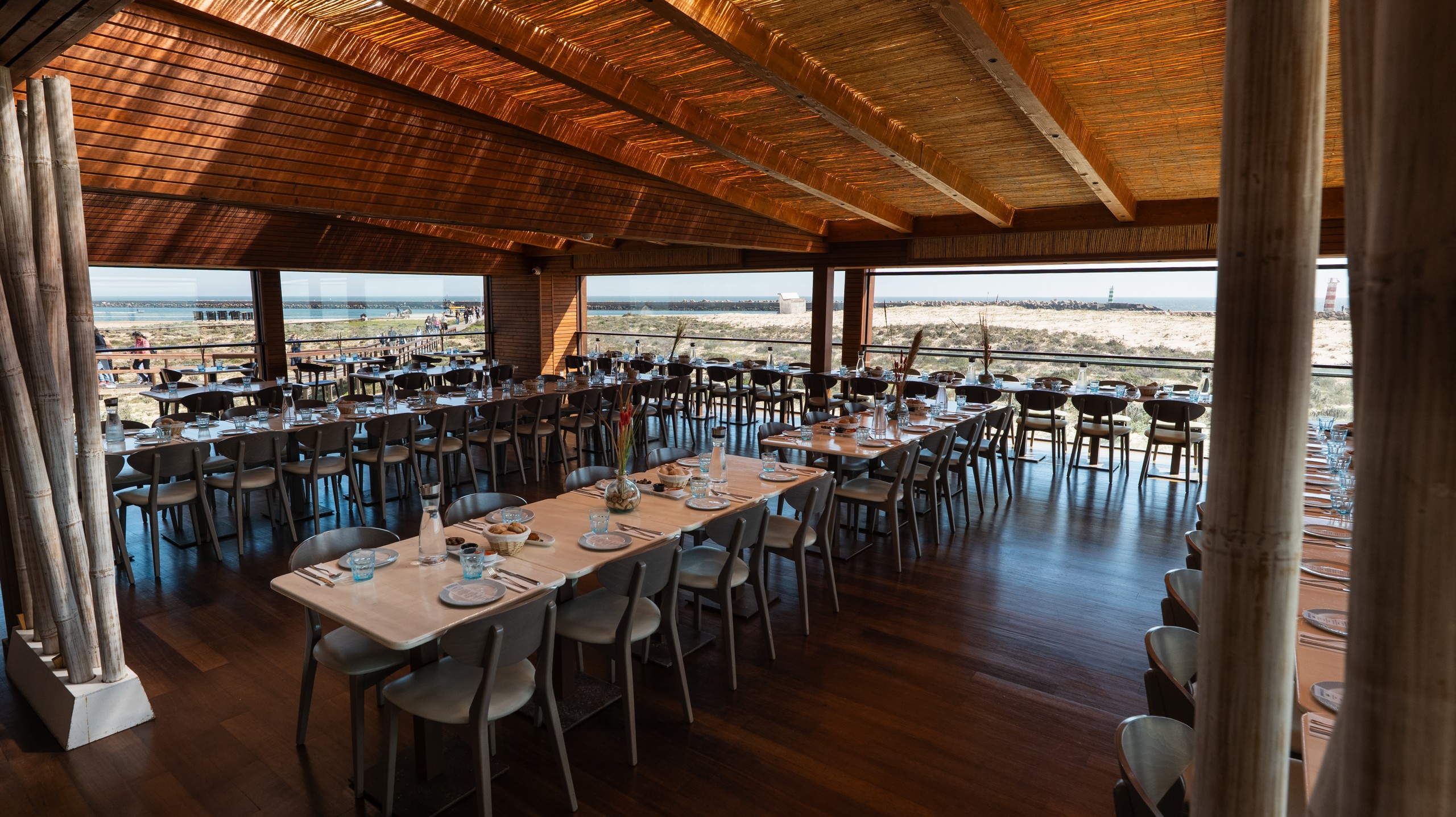Spacious wooden restaurant with view of the beach, set for dining.
