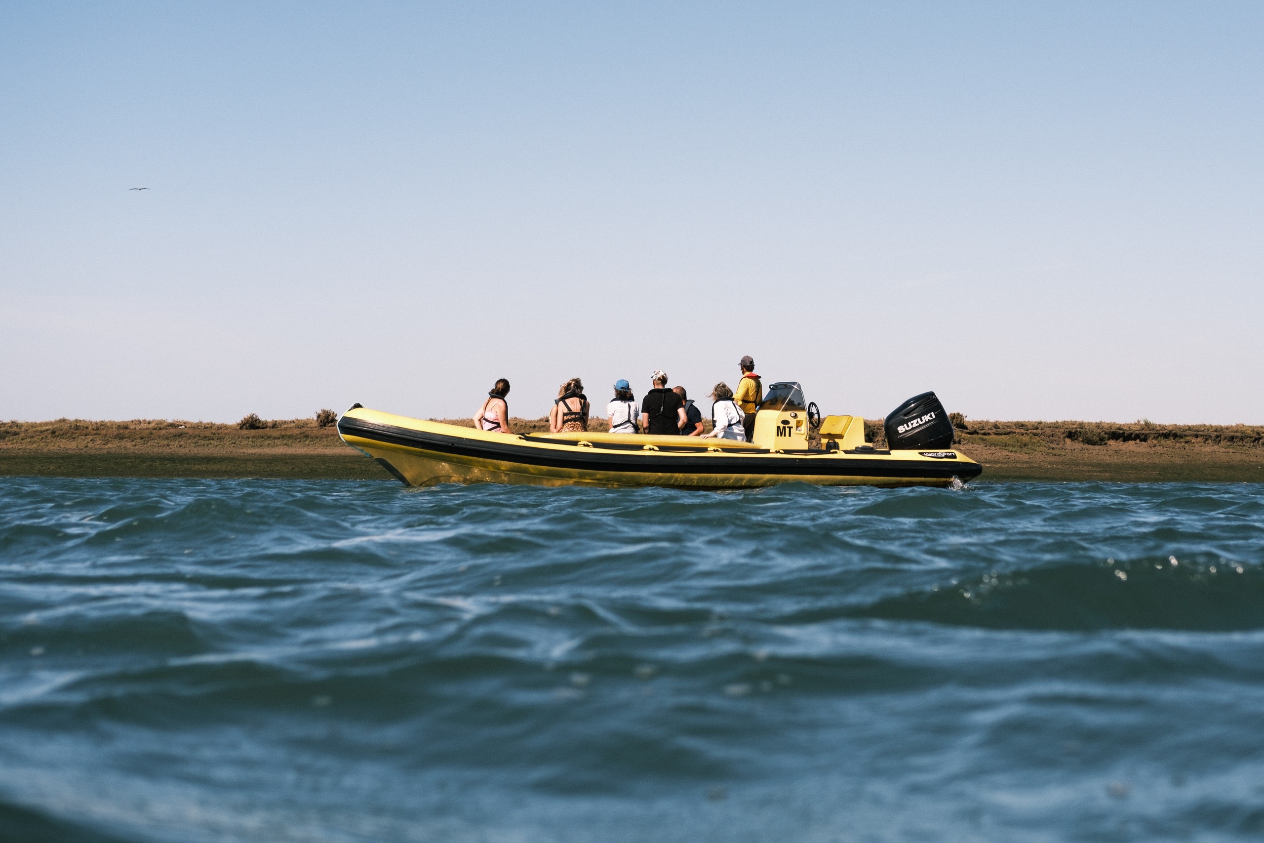 People on a yellow inflatable boat on water with a shoreline in the background.