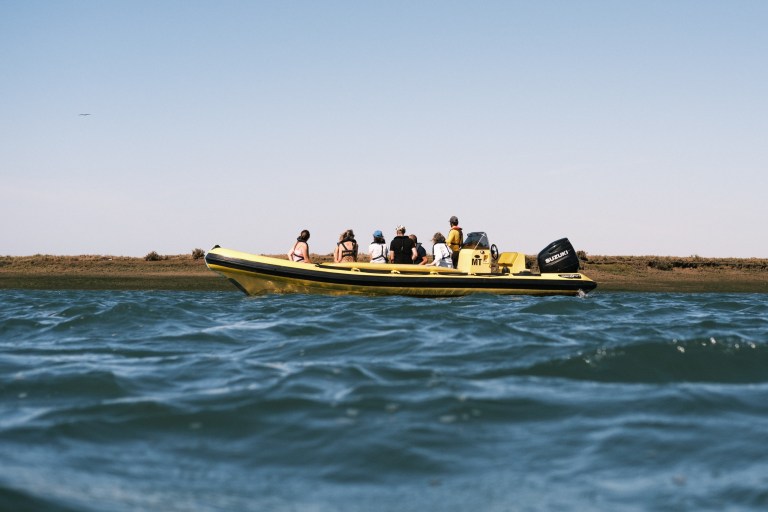 People on a yellow inflatable boat on water with a shoreline in the background.