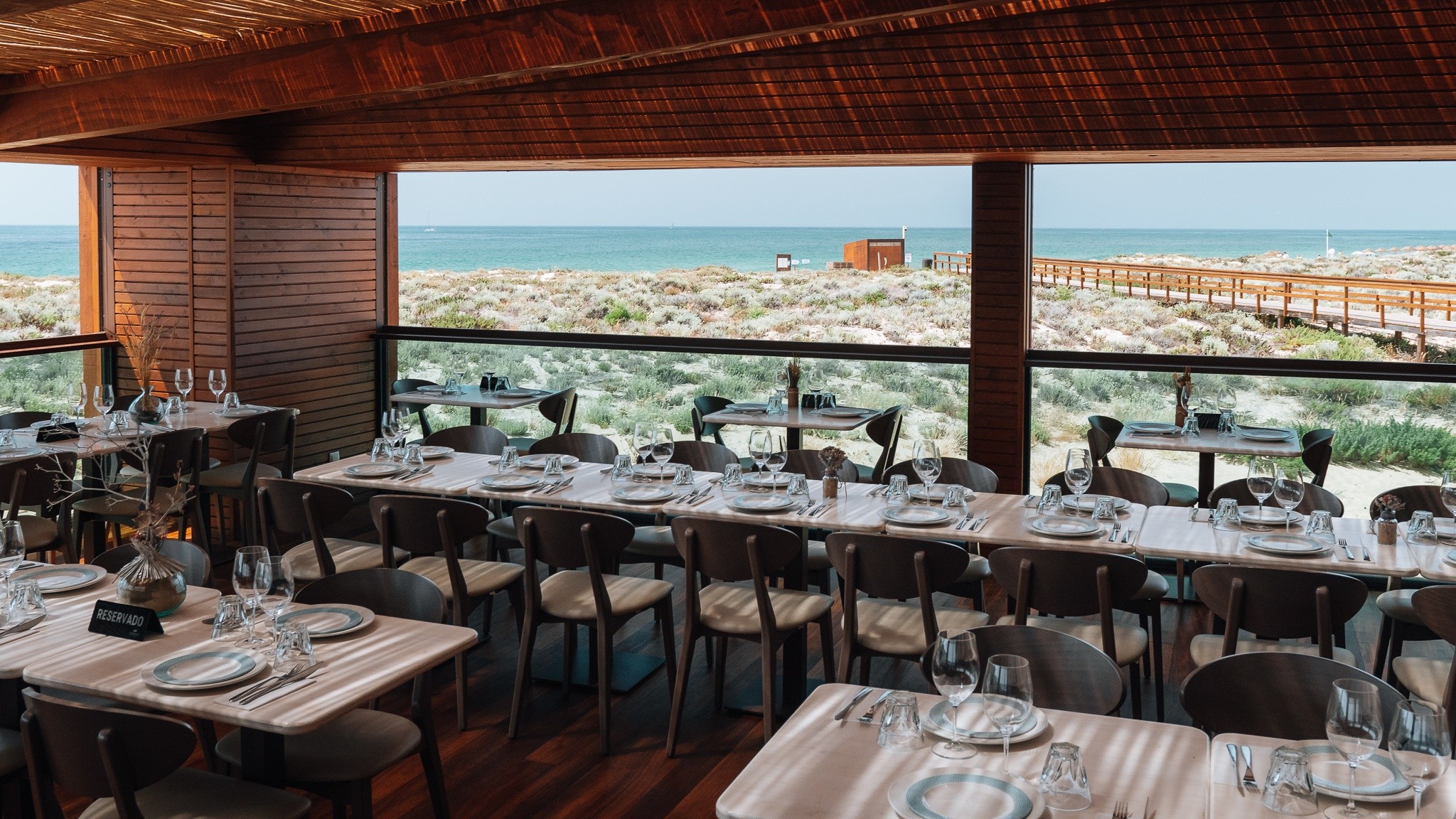 Restaurant with ocean view, wooden interior, tables set for dining.