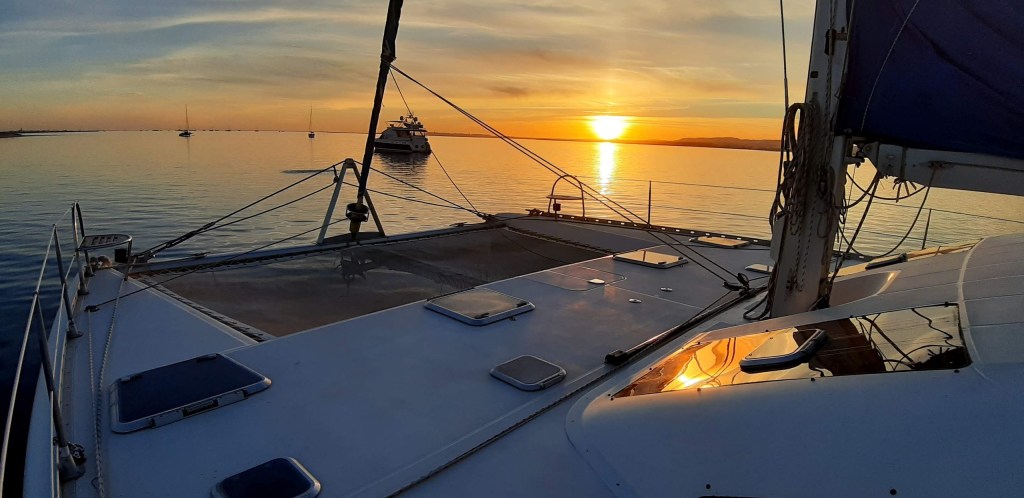 Sunset view from a boat deck on calm water with distant boats.