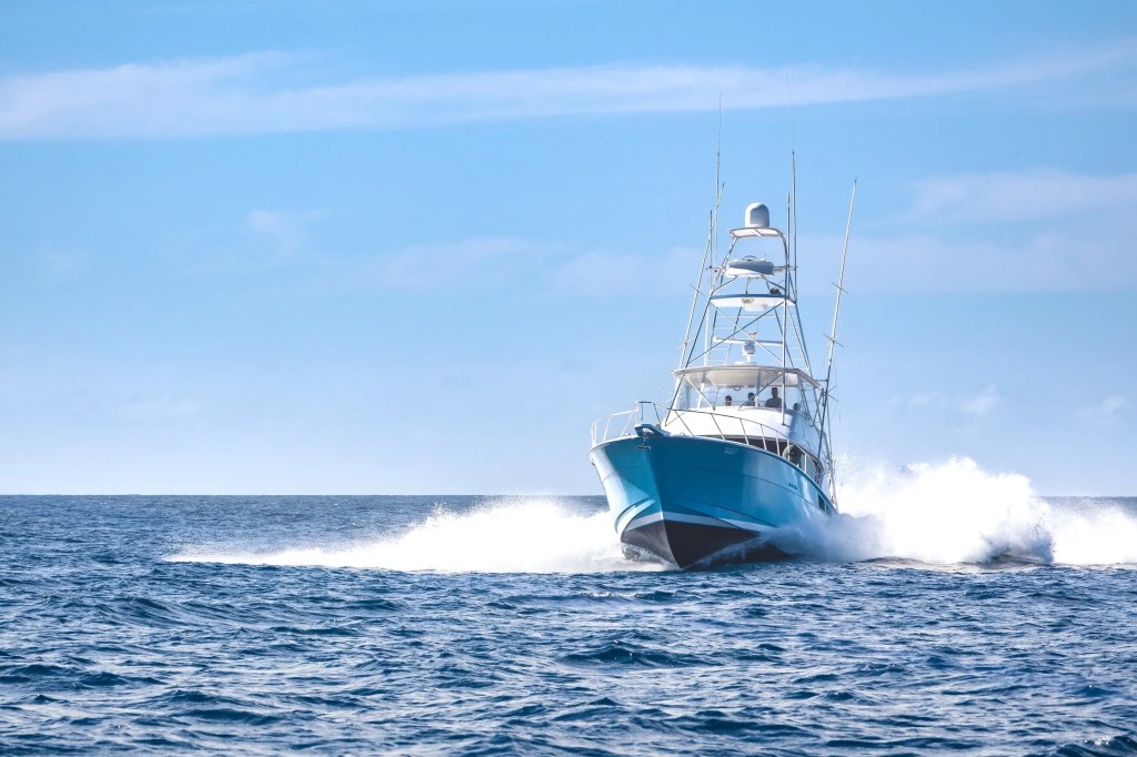 A boat with tall masts moves quickly over ocean waves under a clear blue sky.
