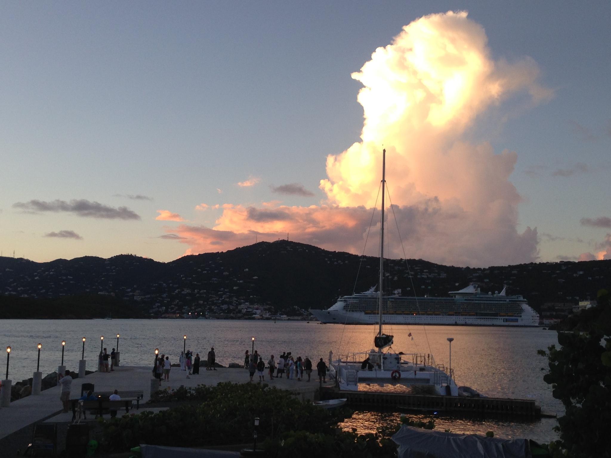 Sunset over harbor with mountains, cruise ship, and people on a dock.