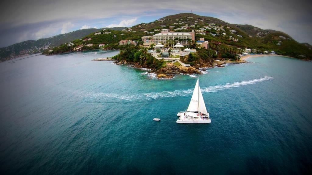 Sailboat on blue ocean near a hilly island with buildings.