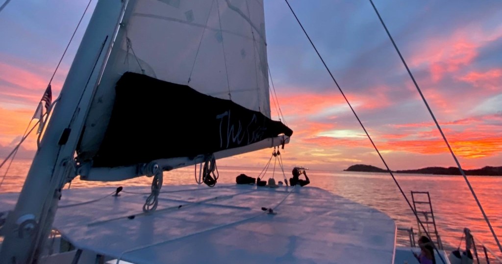 Silhouetted sailboat at sunset with vibrant pink and orange sky.