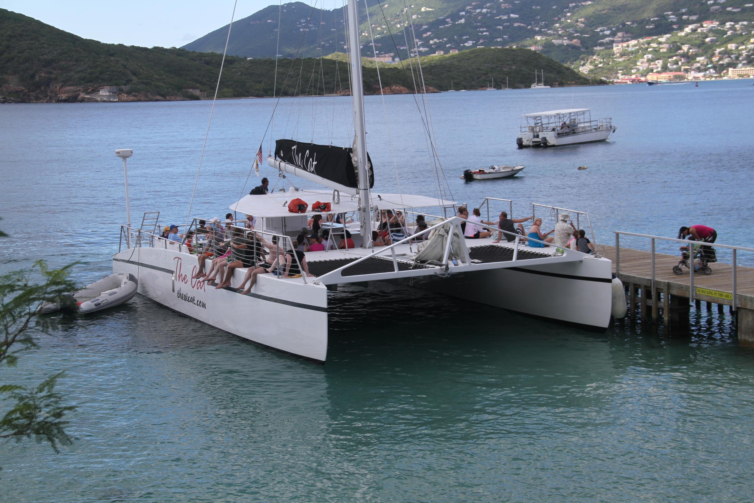 Catamaran docked near shore with mountains in background.
