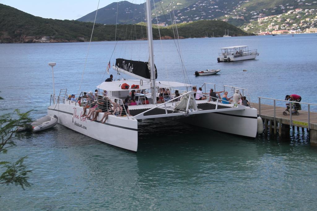 Catamaran docked near shore with mountains in background.