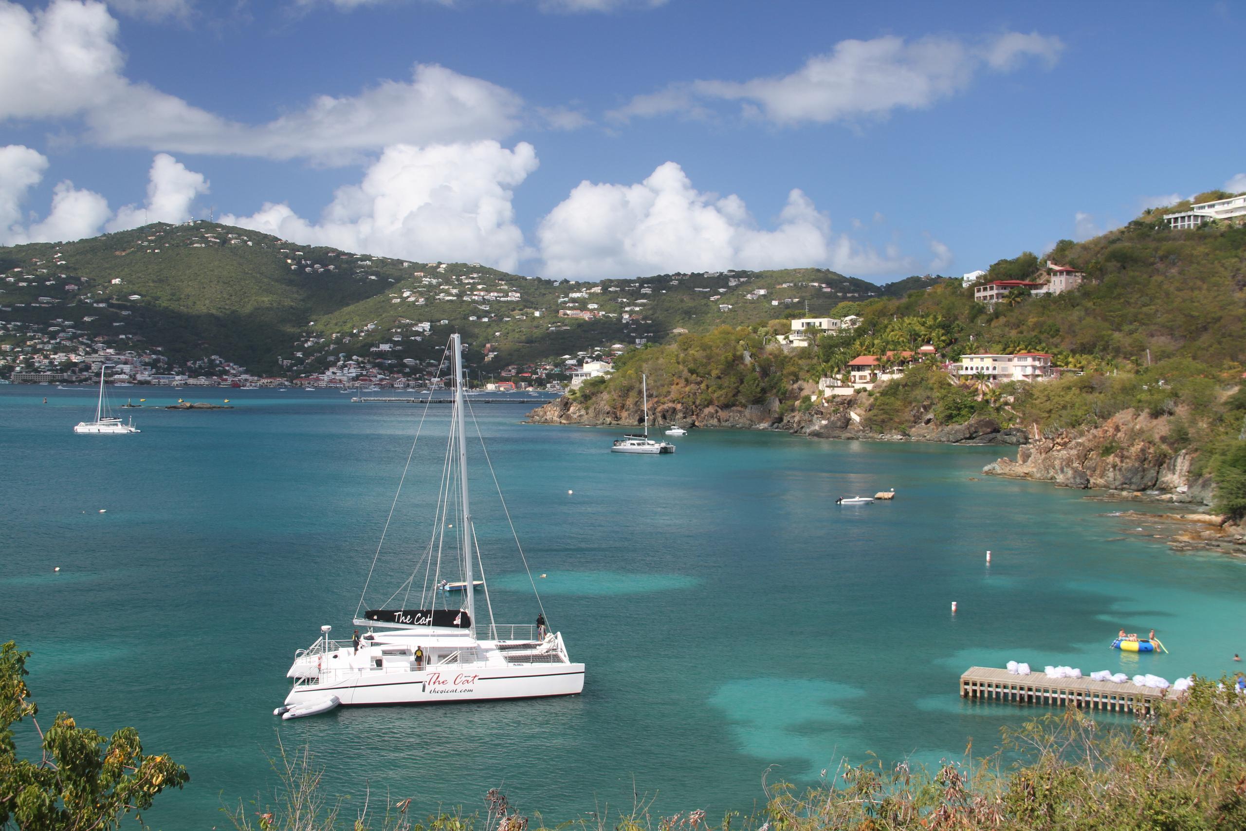 Scenic bay with sailboats, clear blue water, and hillside houses.