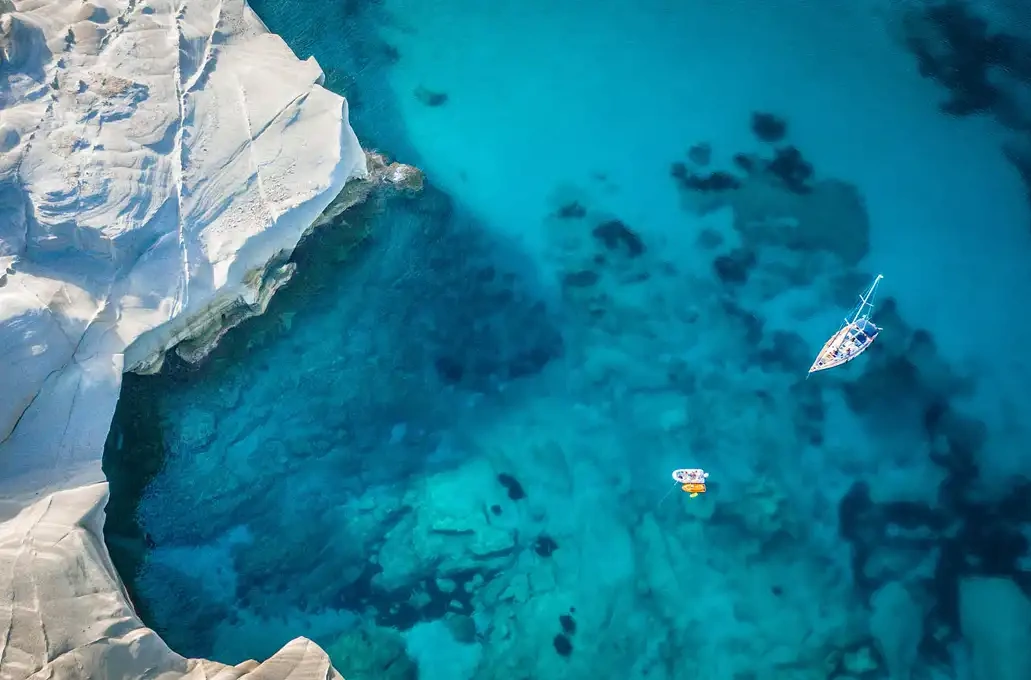 Aerial view of a boat and kayak on clear blue water near white rocky cliffs.