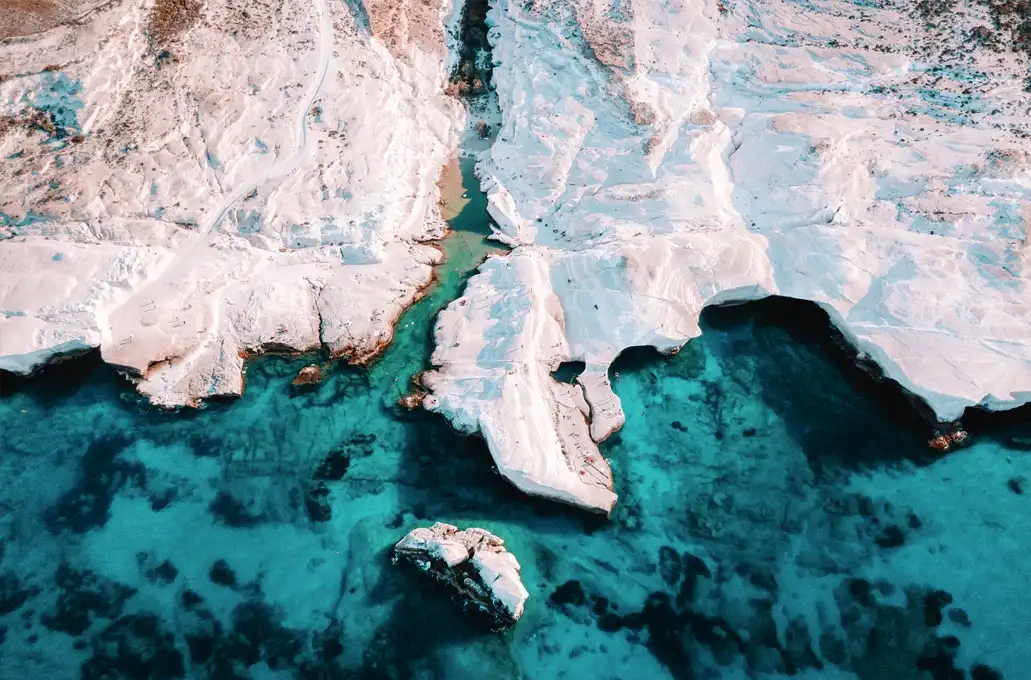 Aerial view of rocky white cliffs and turquoise sea with shadow patterns.