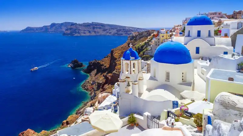 Santorini landscape with white buildings and blue domes overlooking the Aegean Sea.