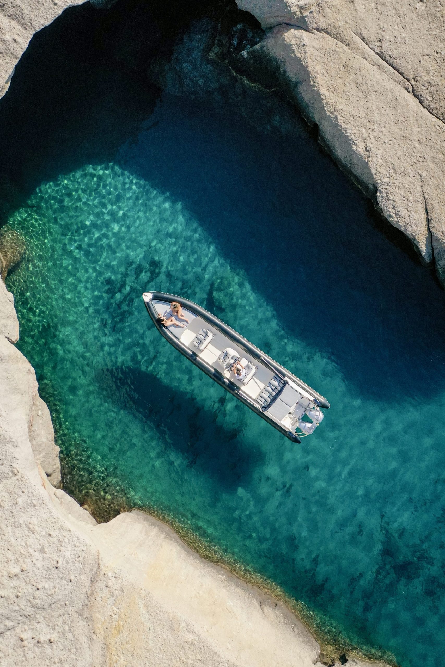 Boat with people in clear blue water surrounded by rocky cliffs.