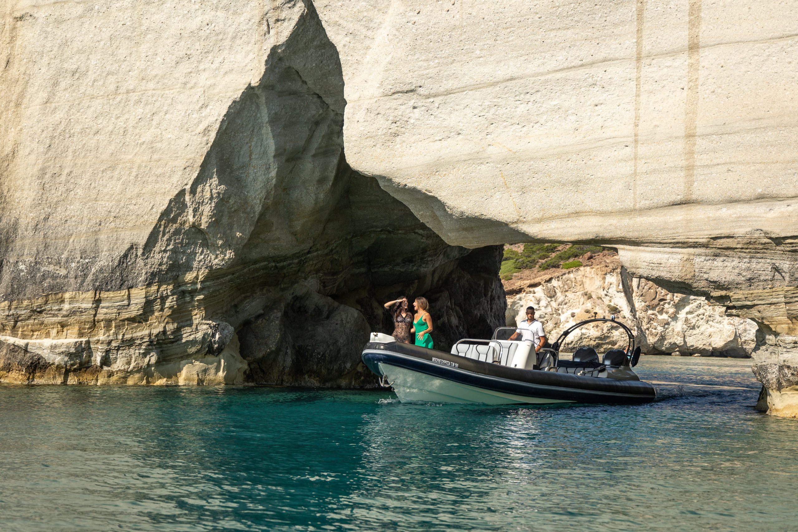 Boat with people exploring a rocky cave on a clear blue sea.