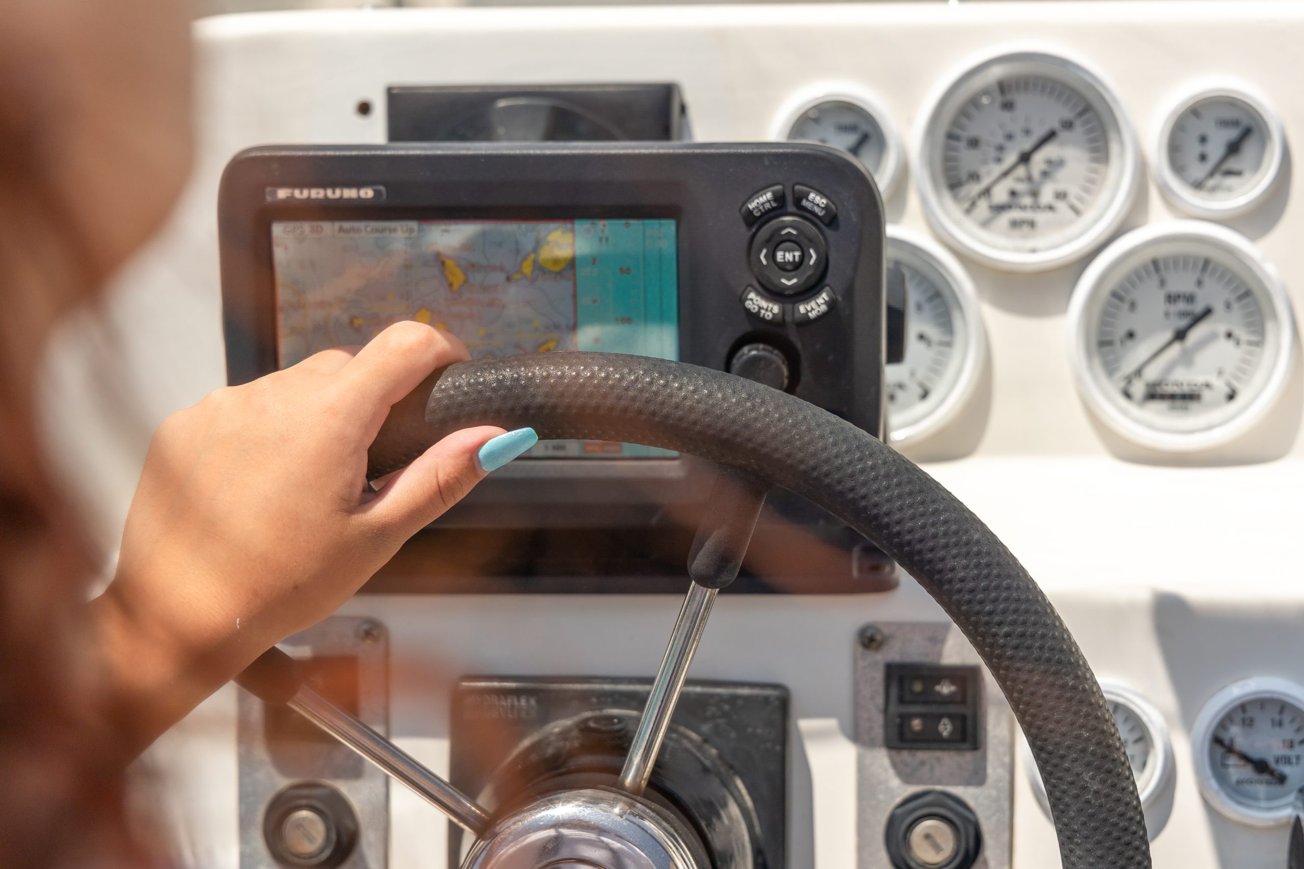 Person steering a boat using a wheel and GPS display.