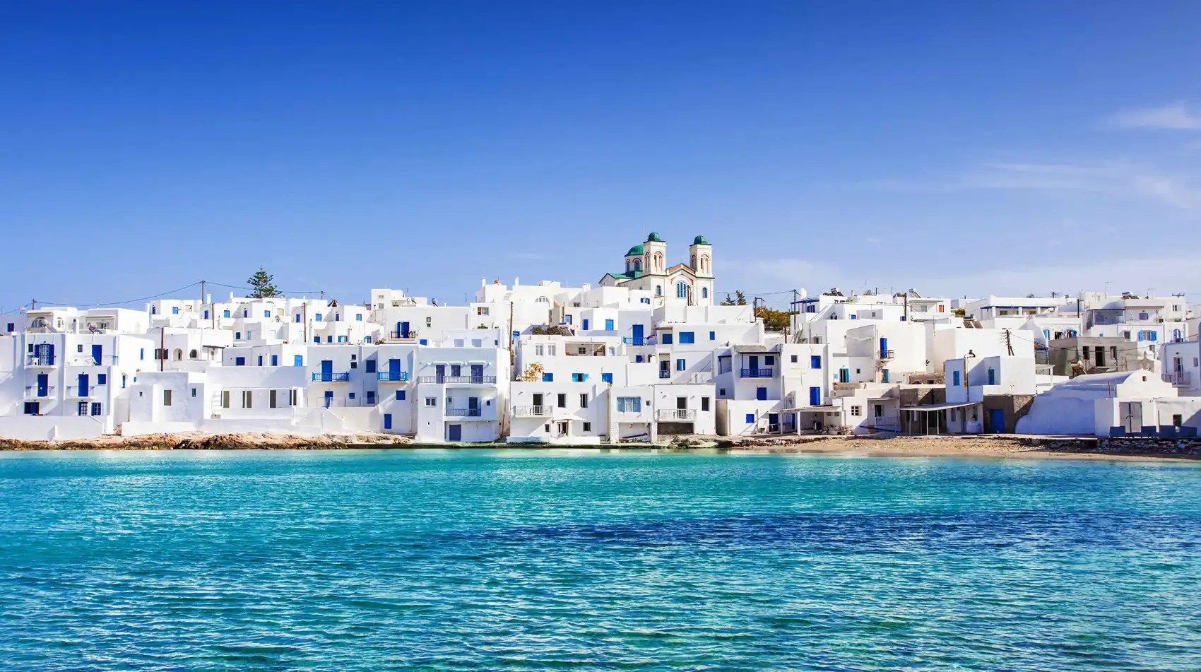 White buildings with blue doors by the sea under a clear blue sky.