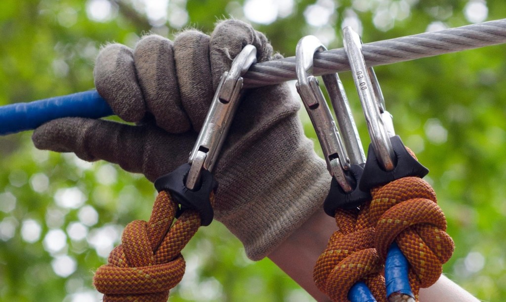 Gloved hand holding onto carabiners attached to a metal cable.
