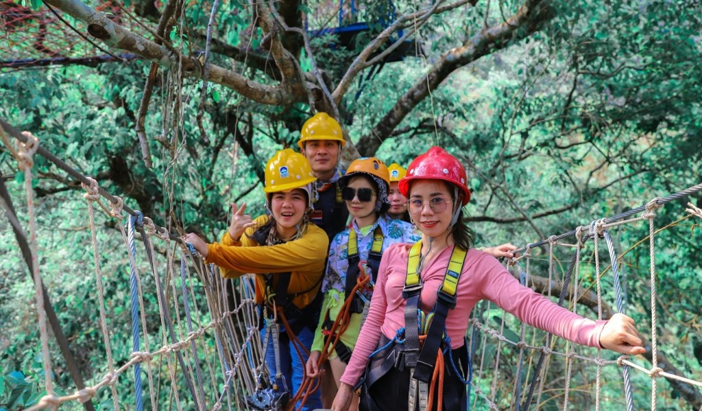 Four people in helmets on a rope bridge in a forested area.