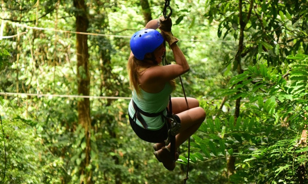 Person zip-lining through a lush green forest wearing a blue helmet.