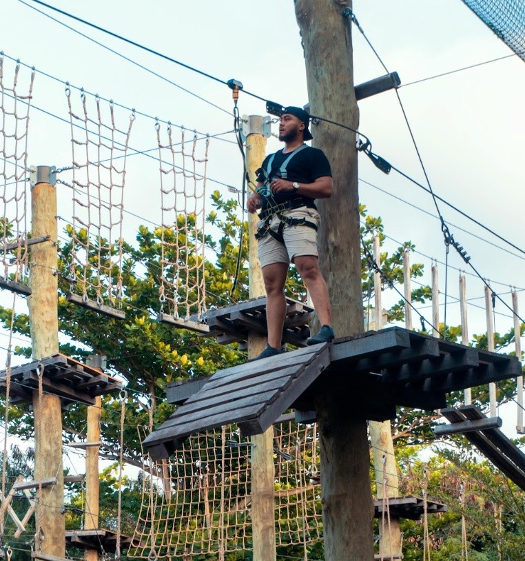 Person on a high ropes course platform, wearing a harness.