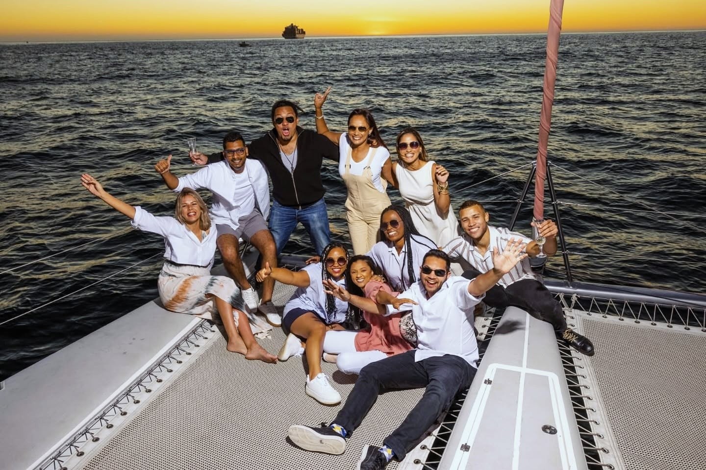 Group of people smiling and posing on a boat at sunset.